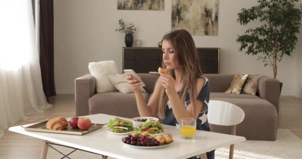 Glamour hermosa hembra sonriente desayunando en casa hablando con smartphone — Vídeos de Stock