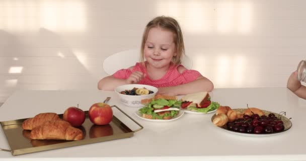 Bedårande barn som har frukost. Två systrar vid frukostbordet. — Stockvideo