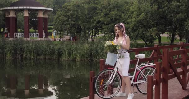 Frau im weißen Kleid blickt im Park in die Kamera — Stockvideo