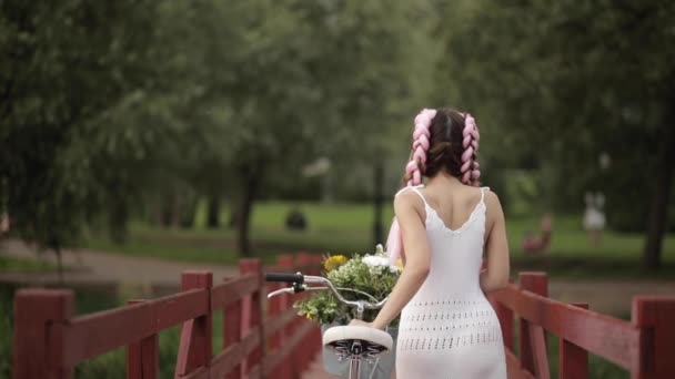 Vista desde la parte posterior de la chica en vestido blanco bicicleta de montar en el parque — Vídeos de Stock