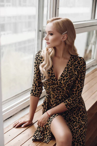 Vonzó nyugodt hölgy leopárd ruhában ül ablakpárkányon — Stock Fotó