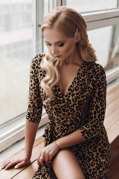 Atractiva dama tranquila en vestido de leopardo sentado en el alféizar de la ventana —  Fotos de Stock