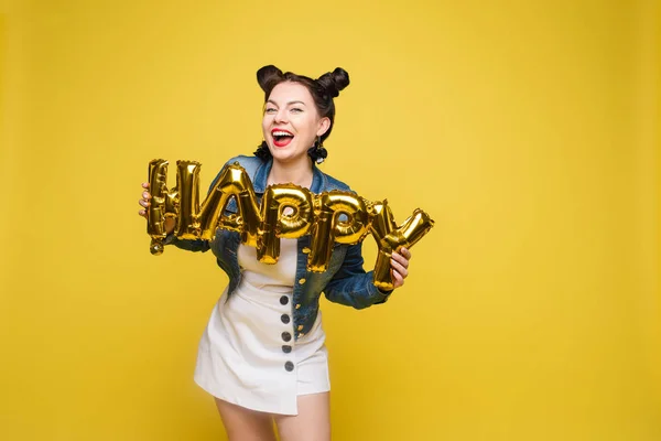 Atrakcyjny szczęśliwy kobieta śmiech trzymając duże złote litery pozowanie na żółtym tle studio — Zdjęcie stockowe