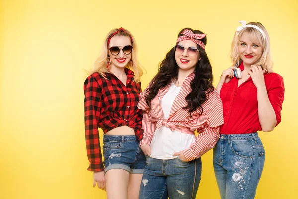 Drie stijlvolle en trendy vriendinnen. Studio shot van trendy meisjes met hoofd bogen, zonnebrillen dragen trendy hipster kleding en glimlachend op de camera. Isoleren op gele achtergrond. — Stockfoto