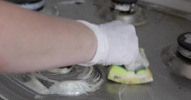 Yakın çekim kadın el giyen eldiven temizliği mutfak sobayı sünger kullanarak