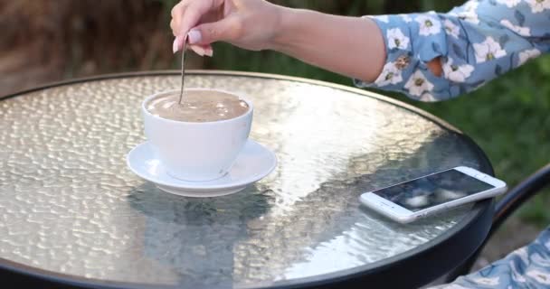 Belarus Minsk 05 26 2019: Unrecognizable woman with mobile stirring coffee with spoon. — Stock Video