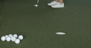Beyaz spor ayakkabılı kadın çimenlerin üzerinde durup golf oynuyor.