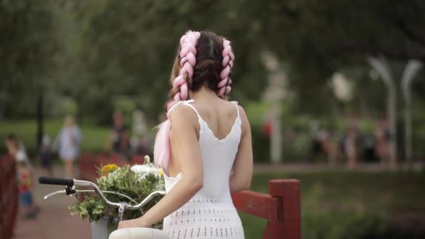 Женщина в белом платье смотрит в камеру во время езды в парке — стоковое видео