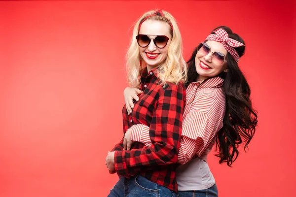Freundliche und trendige Mädchen, die sich auf rotem Hintergrund umarmen. — Stockfoto