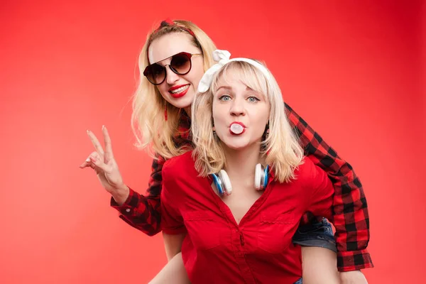 Soeurs avoir du plaisir à donner piggyback.Stock portrait studio de deux copines ou sœurs gaies et positives à la mode s'amuser . — Photo