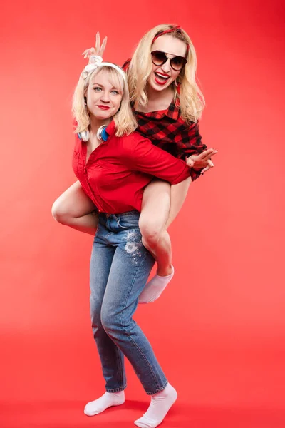 Friendly and trendy girls hugging over red background. Stock Picture