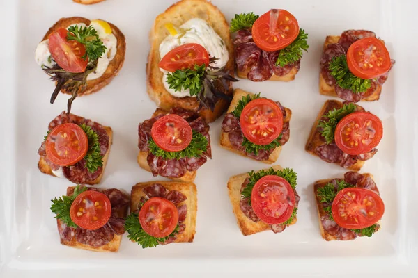 Delicious canape with sausage and tomato.Canapes on white ceramic plates at wedding reception. — Stock Photo, Image