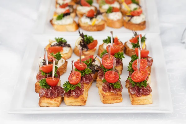 Vynikající konvici s klobásou a rajčatem.Canapes na bílých keramických talířích na svatební hostině. — Stock fotografie