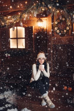 Esmer şapkalı kar yağışı altında ahşap sundurma üzerinde sıcak içecekle.