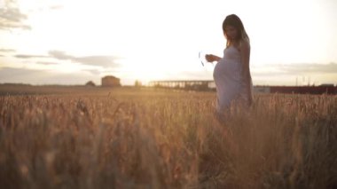 Arazide beyaz elbiseli hamile esmer kadın..