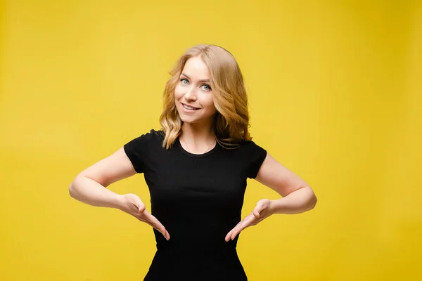 Pretty Caucasian woman with light wavy hair in a black t-shirt, blue pants holds her hands on her waist and smiles in the studio — Stock Photo, Image