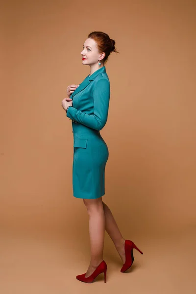 Smiling fashionable woman with red hair in green dress and heels.