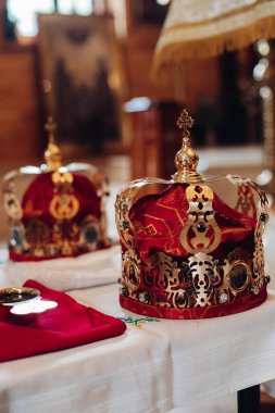 Bebeğin vaftiz töreninden önce kilisedeki bir masada altın ve kırmızı kumaşlı iki güzel taç duruyor.