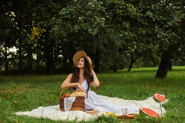 Porträt eines jungen schönen Mädchens mit sogar weißen Zähnen, einem schönen Lächeln im Strohhut und langem weißen Kleid beim Picknick im Garten — Stockfoto