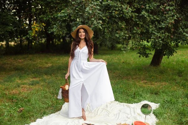 Porträt eines jungen schönen Mädchens mit sogar weißen Zähnen, einem schönen Lächeln im Strohhut und langem weißen Kleid beim Picknick im Garten — Stockfoto