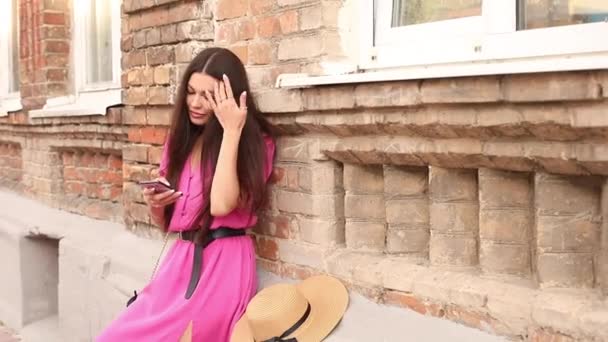 Hermosa joven feliz se sienta cerca de un edificio viejo y charlar con su novio o familia — Vídeo de stock