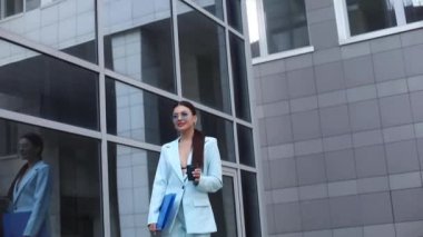 Güzel bir yüzü ve ince bir vücudu olan genç bir kadın ofisin yanında yürüyor ve kahve içiyor.