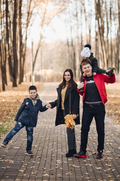 Família caucasiana vai dar um passeio no parque de outono com duas crianças — Fotografia de Stock