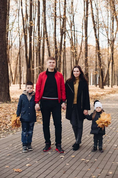 Família caucasiana vai dar um passeio no parque de outono com duas crianças — Fotografia de Stock