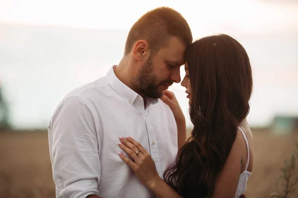 Mujer bastante caucásica con el pelo largo y ondulado oscuro en abrazos de vestido blanco con hermoso hombre en camiseta blanca y pantalones cortos —  Fotos de Stock