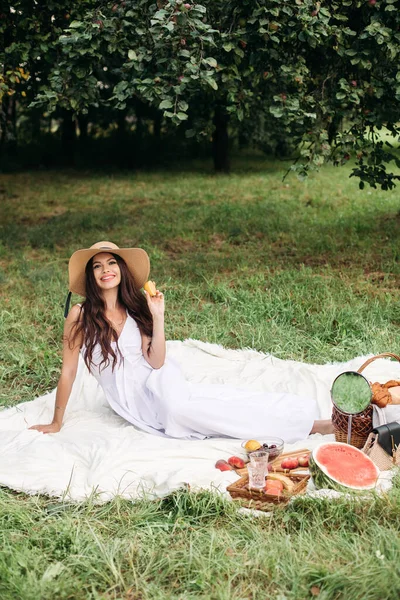 Porträt eines jungen schönen Mädchens mit sogar weißen Zähnen, einem schönen Lächeln im Strohhut und langem weißen Kleid beim Picknick im Garten — Stockfoto