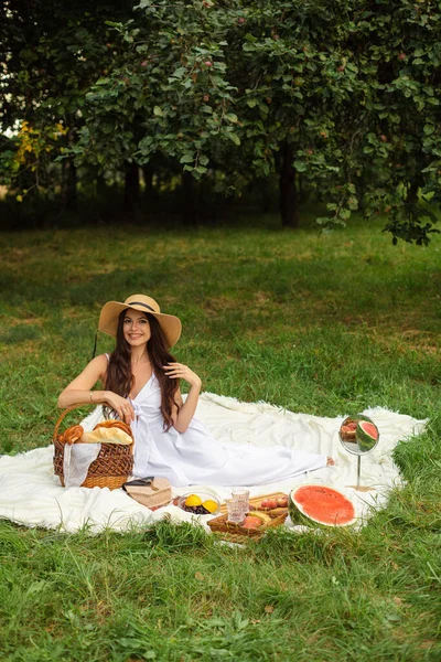 白い歯を持つ若い美しい少女の肖像画、わらの帽子と長い白いドレスの美しい笑顔は庭にピクニックを持っています — ストック写真