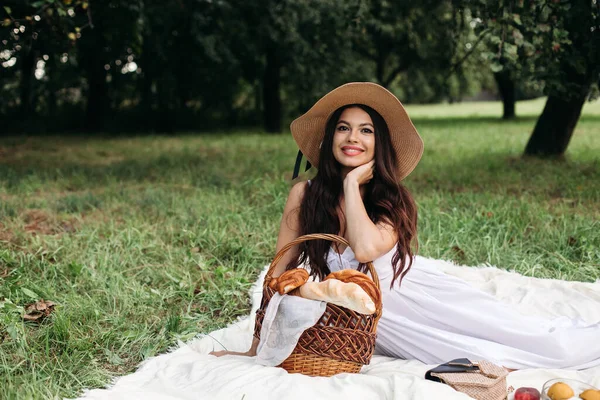 Porträt eines jungen schönen Mädchens mit sogar weißen Zähnen, einem schönen Lächeln im Strohhut und langem weißen Kleid beim Picknick im Garten — Stockfoto