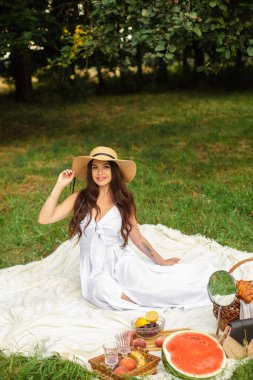 Beyaz dişli güzel bir kızın portresi, hasır şapkalı güzel bir gülümseme ve uzun beyaz bir elbise bahçede piknik yapıyor.