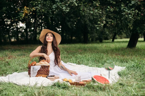 Porträt eines jungen schönen Mädchens mit sogar weißen Zähnen, einem schönen Lächeln im Strohhut und langem weißen Kleid beim Picknick im Garten — Stockfoto