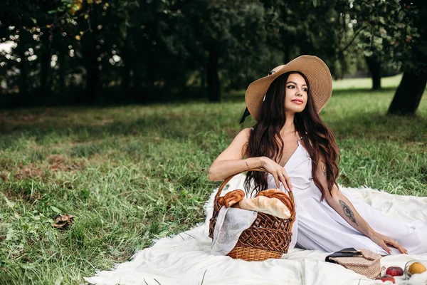 Porträt eines jungen schönen Mädchens mit sogar weißen Zähnen, einem schönen Lächeln im Strohhut und langem weißen Kleid beim Picknick im Garten — Stockfoto