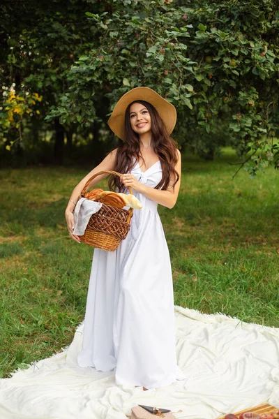 Retrato de uma jovem menina bonita com dentes brancos, um belo sorriso em um chapéu de palha e vestido branco longo fazer um piquenique no jardim — Fotografia de Stock