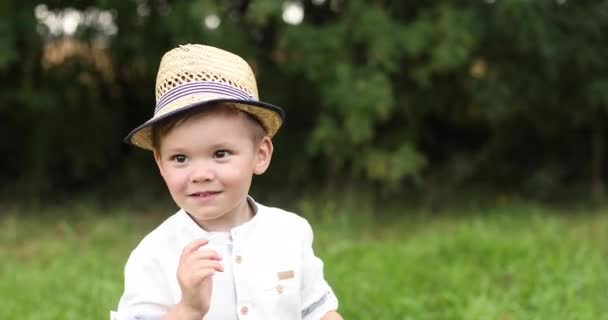 Χαμογελώντας ντροπαλό Καυκάσιο παιδί με ψάθινο καπέλο κοιτώντας μπροστά — Αρχείο Βίντεο