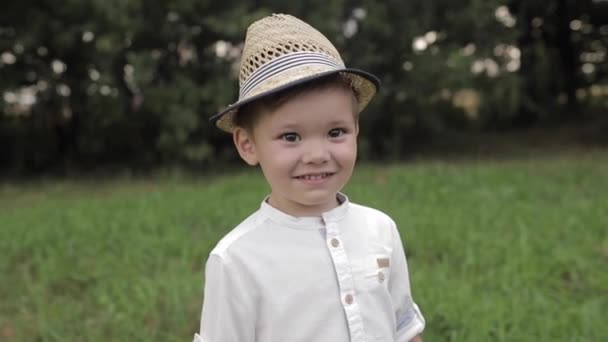 Sorridente timido bambino caucasico in un cappello di paglia guardando avanti — Video Stock