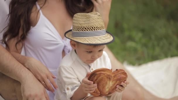 一个长着漂亮脸蛋的白人小男孩在公园里吃着一个美味的面包 — 图库视频影像