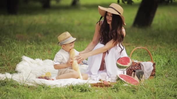 Młoda piękna kobieta daje bagietkę swojemu dziecku na pikniku w parku latem — Wideo stockowe