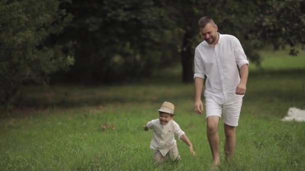 Tata bawi się z synem w ogrodzie, dziecko upada, ale nadal się śmieje. — Wideo stockowe