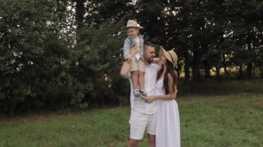 Kısa siyah saçlı, beyaz tişörtlü ve şortlu yakışıklı bir baba, uzun siyah dalgalı saçlı, uzun beyaz elbiseli çekici bir anne...