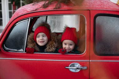 Gülümseyen tatlı kış çocuğu ve kırmızı şapkalı kızlar arabada oturmuş eğleniyorlar.
