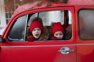 Gülümseyen tatlı kış çocuğu ve kırmızı şapkalı kızlar arabada oturmuş eğleniyorlar.
