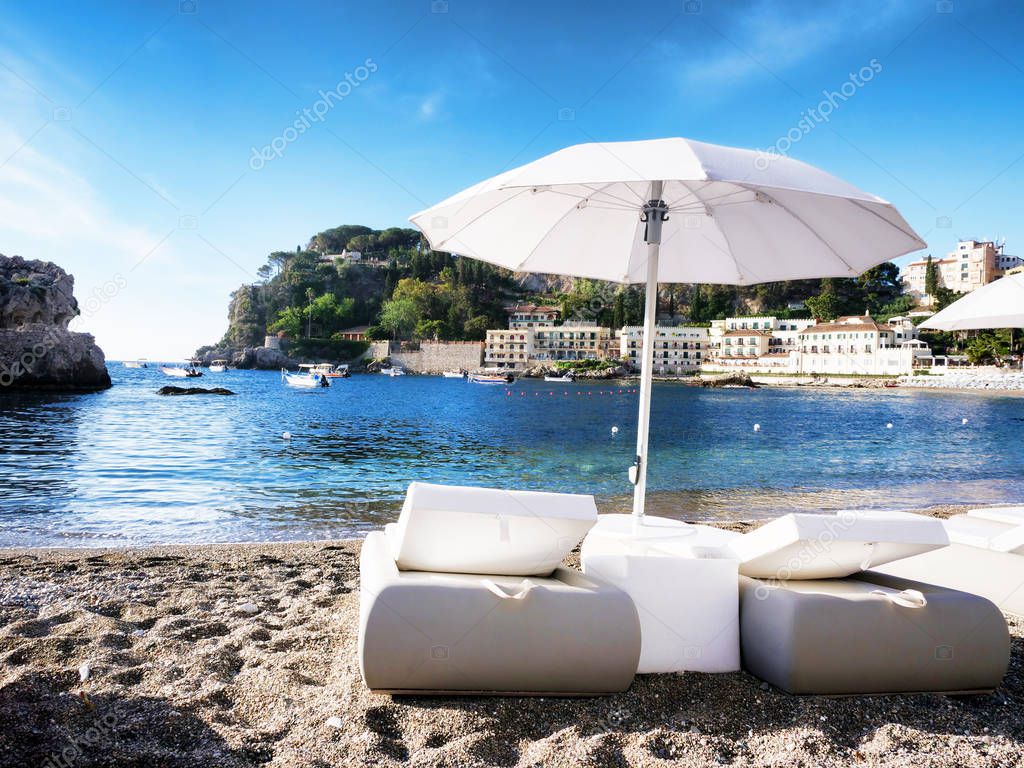 White elegant Sunbeds for romantic vacation at Mazzaro beach in Sicily Italy with hotels on the waterline and boats at the background