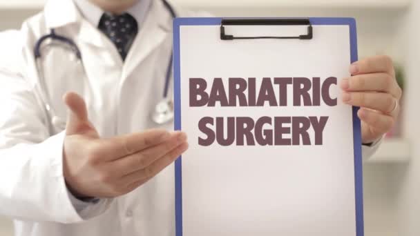 Doktor se stetoskopem ukazujícím na schránku s titulem BARIATRIC SURGERY jako diagnózou — Stock video