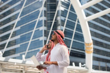 İki Arap işadamı kullanım dizüstü bilgisayar ve cep telefonu büyük şehirde gökdelenler içinde belgili tanımlık geçmiş ile iş bölgesi. Resim için kısa mesaj ekleyin. Tasarım sanat çalışmaları için fon.