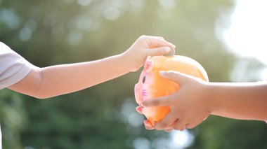 El kumbara tutarak ve paralar, ağır çekim koyarak çocuk. Bokeh arka plan. Para tasarrufu ve gelecek için para toplama.
