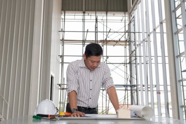 Asyalı erkek mühendisler planları bir inşaat alanında bir masada bakarak. Mimar veya planlayıcısı kavramı