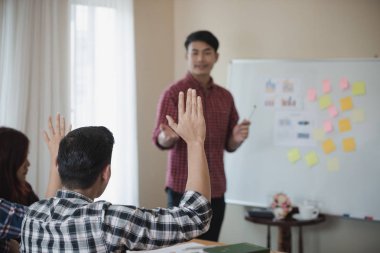 Soru sormak için bir el kaldırma ekose gömlek giymiş genç bir Asyalı adam ve bir konferans salonu, bir iş.